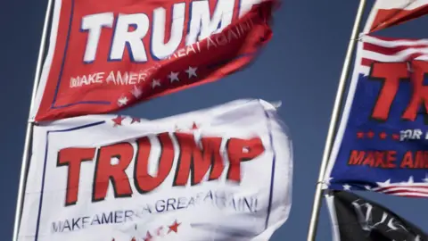 A stock image of three flags that say Trump and Make America Great Again waving in the wind.