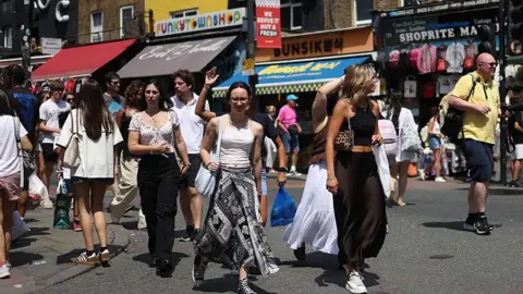 A crowd of young people on a pedestrianised shopping street, wearing summery clothes on a sunny day.
