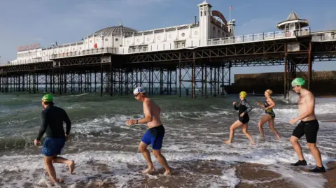 Getty Images Swimmers running into the sea next to Brighton Pier