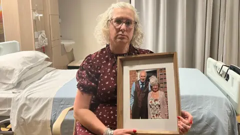 Ashgate Hospice Julie Whittaker wearing a maroon pattern top, holding a framed picture of her parents