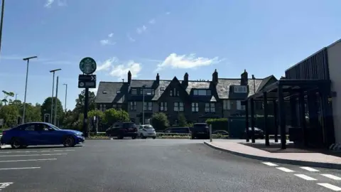 Julia Bryson/BBC A car park in front of a row of terraces houses with a tall Starbucks sign in front.