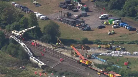 The scene at the derailment site, with the overturned carriages and a series of cranes and workmen near and on the tracks