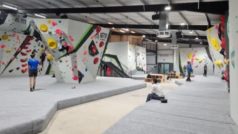 270 Climbing Park The indoor climbing centre which has white walls in jagged irregular shapes and slopes, with bright colourful handles where people can grab onto and climb. 