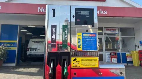 A petrol pump with two fuel nozzles, one marked diesel and the other for unleaded petrol on a garage forecourt in Guernsey.