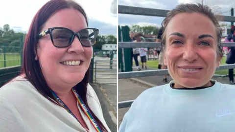BBC/Andy Watson To the left is Emma Gardner, a smiling middle-aged woman with dyed red-purple hair, wearing sunglasses and a white top, with a Pride-patterned NHS lanyard around her neck. To the right is Sarah Stokoe. She is smiling and has tied-back brown hair. She wears a light blue sweatshirt. Behind them is the entrance to Hazlewood School.