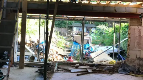 Nick Marns A very messy scene of building work carried out by Steve Figg. The back of the house has been totally gutted and is being propped up by poles. The garden is covered in lots of rubble and general waste from the project.