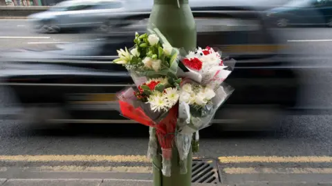 A bouquet of flowers attached to a lamppost next to a busy road