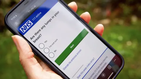 CUH/NWAFT A person is holding a phone which is on the NHS 111 online service. It has a multiple choice question which reads: Are there any lumps in your breast?