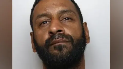 A mugshot of Ansar Younis, who has short black hair and a beard.