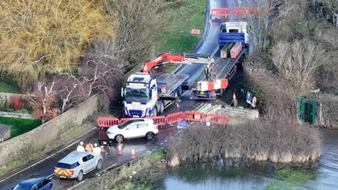 Eddie Mitchell Two lorries can be seen within the road closure. There are other vehicles in the drone image. 