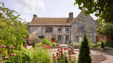 Poole Museum An ornate garden behind Scaplen's Court, a two-storey historical building. The garden has sculptured hedges, paving and trees,