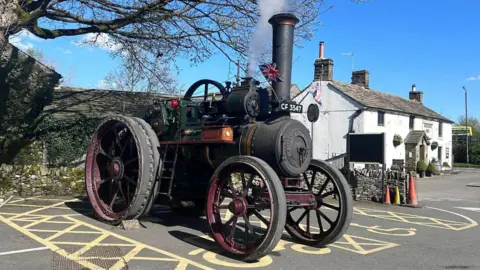 Rachel Rennie A green traction engine with red wheels parked in a parking bay outside a rural pub.