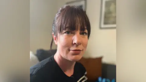 Kim Russell, who has dark hair in a ponytail and fringe, looks at the camera wearing a black t shirt.