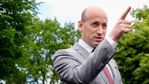 Stephen Miller points while speaking, wearing a grey suit