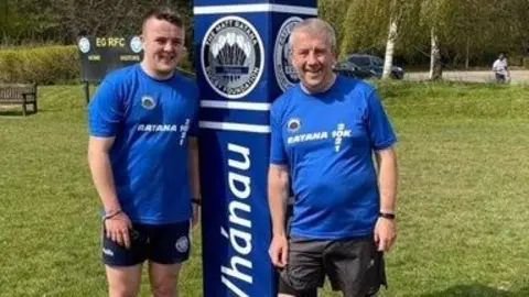 Family photo Henry and Antony Weller standing on a rugby pitch in Matt Ratana Rugby Foundation kit.