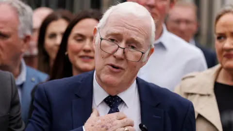 PA Media Eugene Reavey speaking to the media outside the Royal Courts of Justice in Belfast. He has shirt white hair, wearing glasses, a navy blazer, white shirt and navy tie. He is holding his right hand to his chest.