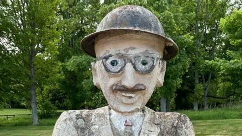 Railtons A statue of a man in what looks like a protective hat with glasses and a moustache wearing a suit and tie