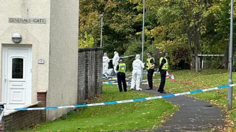 Uniformed police officers and forensic officers in white overalls standing outside a taped-off house on General's Gate
