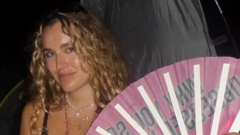 Hermione La Chapelle A woman with blonde wavy hair stares at the camera. 