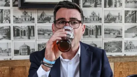 PA Media The new prime minister wears a suit in a pub and drinks a beer from a pint glass. 