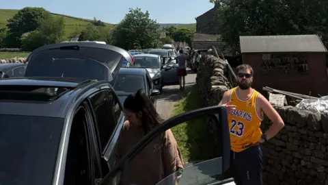 A large number of cars parked on a small lane in a village in the Yorkshire Dales