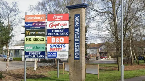 Google A sign is shown just off centre to the left, with the shops which are at Forest Retail Park in Thetford. In the background you can see parts of the retail complex. 