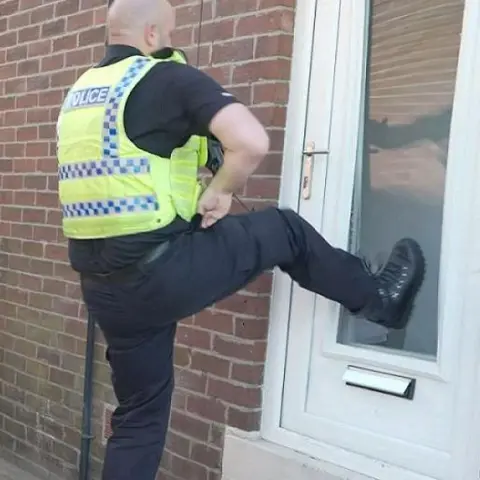 Northumbria Police Northumbria Police officer kicking in a white UPVC door with a clear central panel