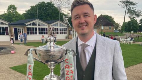 Kyren Wilson wearing a grey jacket and holding a big silver trophy at Wicksteed Park