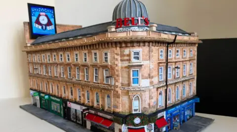 A cardboard model of Union Corner. It is a Victorian Building with colourful shop fronts on the ground floor.
