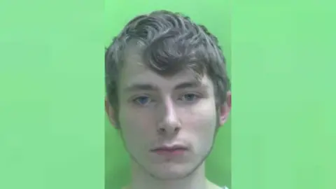 Headshot of Jordan Hutchinson who has short brown hair against a green background.