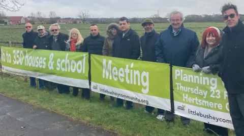 Justin Dealey/BBC Campaigners standing by a sign against a housing development in Little Bushey