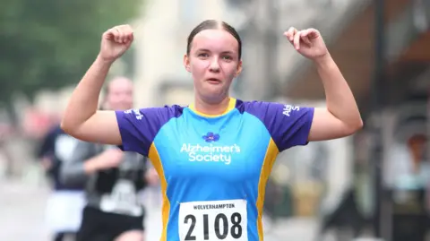 Wolverhampton Half Marathon and 10k A woman in a blue top raises her arms in celebration as she looks at the camera