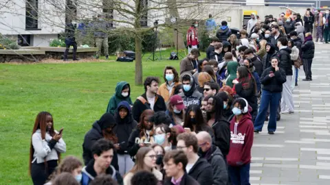 Getty Images A large queue of young people. Some are wearing masks. 