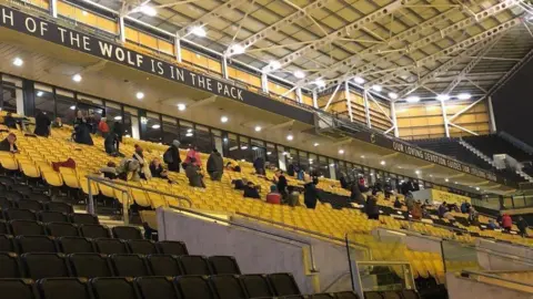 Wolverhampton Wanderers Seats in a football stadium, in blocks of yellow and black, with people sitting in some of them