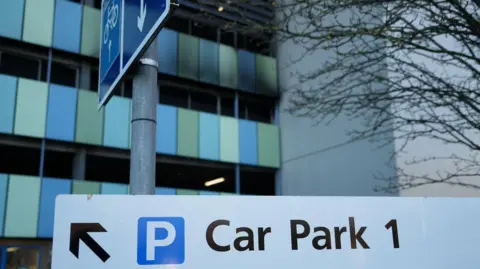 Shaun Whitmore/BBC Part of the outside of a car park shows black charring on green and blue panels and a wall.