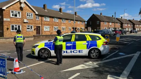 Sam Read/BBC Two police officers standing in a street, by a police car, with their back to the camera
