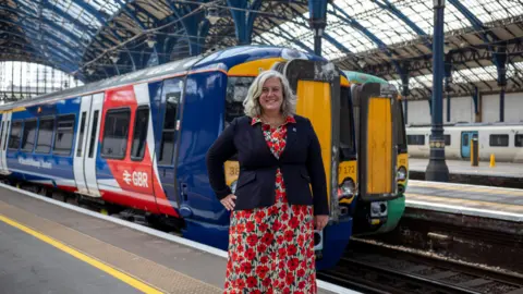 Getty Images Woman in dress with poppies in front of two trains, one in blue white and red, another green and yellow 