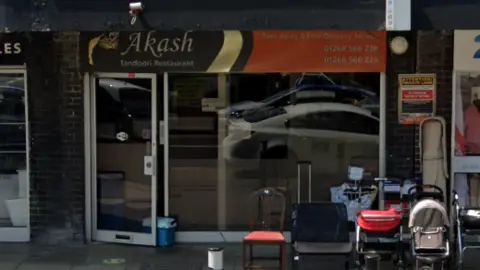 The outside of the Akash Tandoori, a restaurant with a glass door and a large glass window with a sign above saying "Akash".