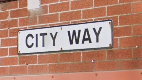 A red brick wall with a white and black street sign that says "City Way"