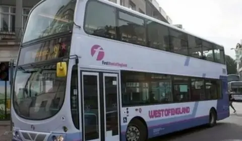 Purple and white First bus travelling along road with another bus in the background.