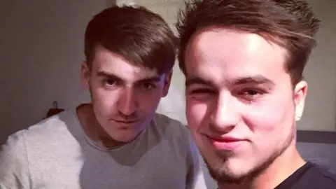 Jordan Wharton Josh, on the left, has short brown hair and brown eyes. He is wearing a grey t-shirt. Next to him, on the right, is Jordan who has brown hair and a thin goaty beard along the jawline. He is wearing a black t-shirt and is winking at the camera.