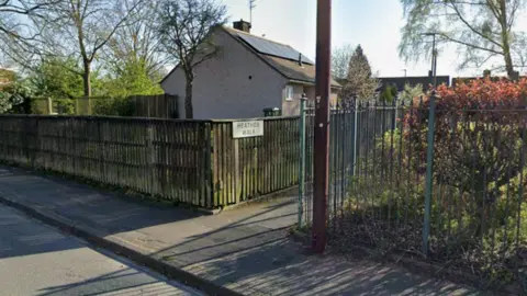 An alleyway running behind someone's house, called Heather Walk. There are moss-covered wooden fences lining the way.