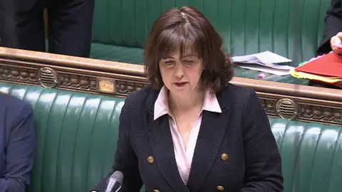 UK Parliament Lucy Powell addressing the House of Commons. She is wearing a blue jacket and the green benches of the Commons are in the background 