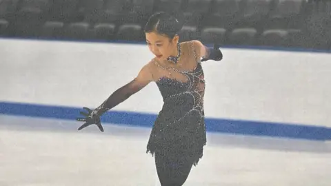 Supplied image Jinna Han, a young woman with black hair, skates in an ice rink wearing a black costume.