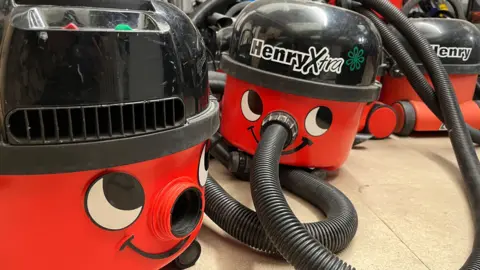 A group of the familiar red smiling Henry vacuum cleaners