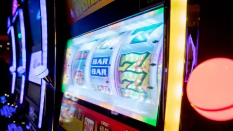 Getty Images We can see the screen of a digital slot machine. It's displaying a traditional style game with three reels where we can see the number 7 and 'Bar'.