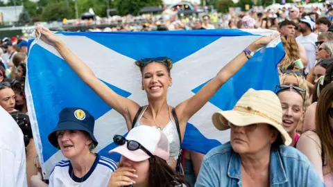 Getty Images A smiling woman holds up a Saltire while in the crowd at a music festival