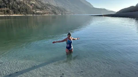 Ellie Bull swimming in a lake whilst on holiday, surrounded by mountains.