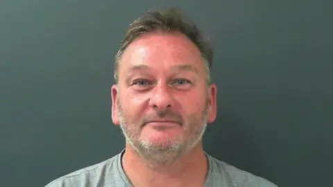 North Yorkshire Police A man with short grey hair and beard wearing a grey T shirt standing against a grey background
