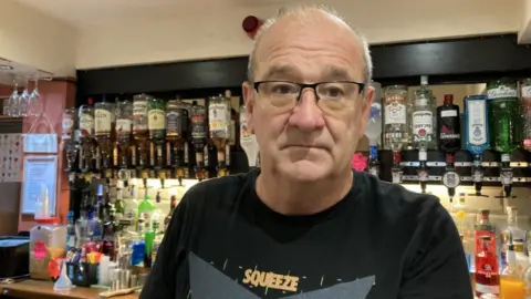 Paul Fitzpatrick, the landlord of the Hare and Hounds pub in Oswaldtwistle, stands behind the bar, in front of the spirits optics